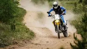 Motorradfahrer auf gelber Suzuki DR-Z4S fährt auf staubigem Weg im Gelände.