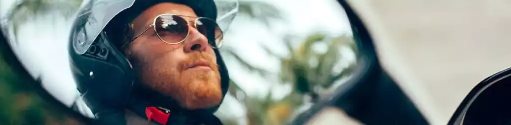 Motorradfahrer mit Helm und Sonnenbrille im Rückspiegel, Palmen im Hintergrund.
