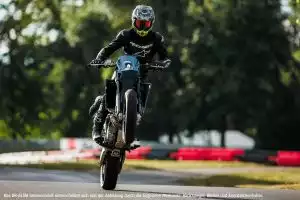 Motorradfahrer auf Suzuki DR-Z4S bei Wheelie auf Rennstrecke im Freien.
