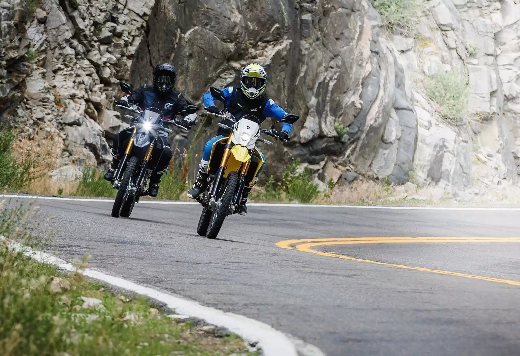 Zwei Suzuki DR-Z4S Motorräder in Gelb und Schwarz auf kurviger Bergstraße.