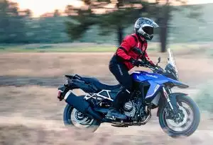 Fahrer auf blauer Suzuki V-Strom 800 im Gelände, in Fahrt mit Staubentwicklung, für ein Abenteuergefühl.