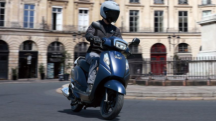 Ein Fahrer auf dem Suzuki Address 125 fährt durch eine historische europäische Innenstadt – wendig, kompakt und ideal für urbane Mobilität.