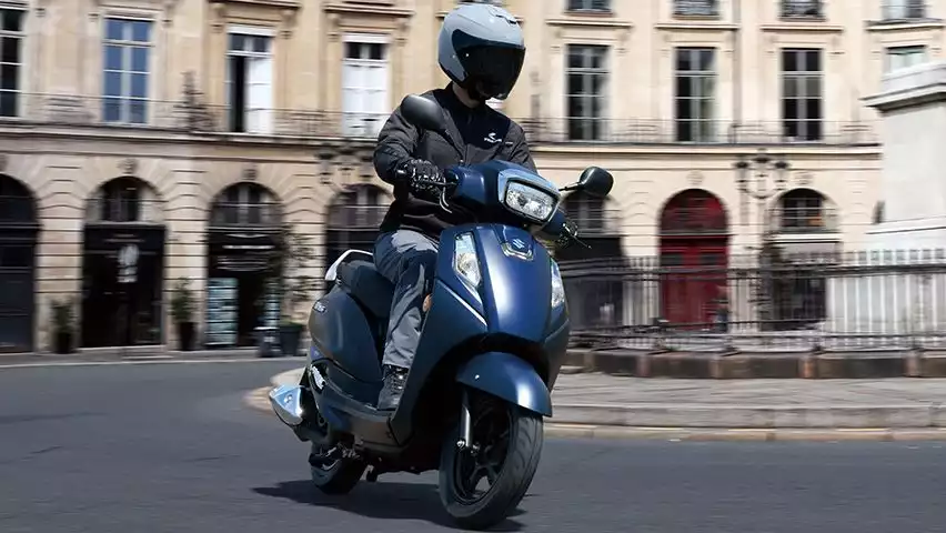 Ein Fahrer auf dem Suzuki Address 125 fährt durch eine historische europäische Innenstadt – wendig, kompakt und ideal für urbane Mobilität.