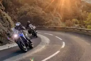 Suzuki V-Strom 800 in Kurve bei Abendlicht, zwei Fahrer auf Bergstraße, Akrapovič Zubehör.