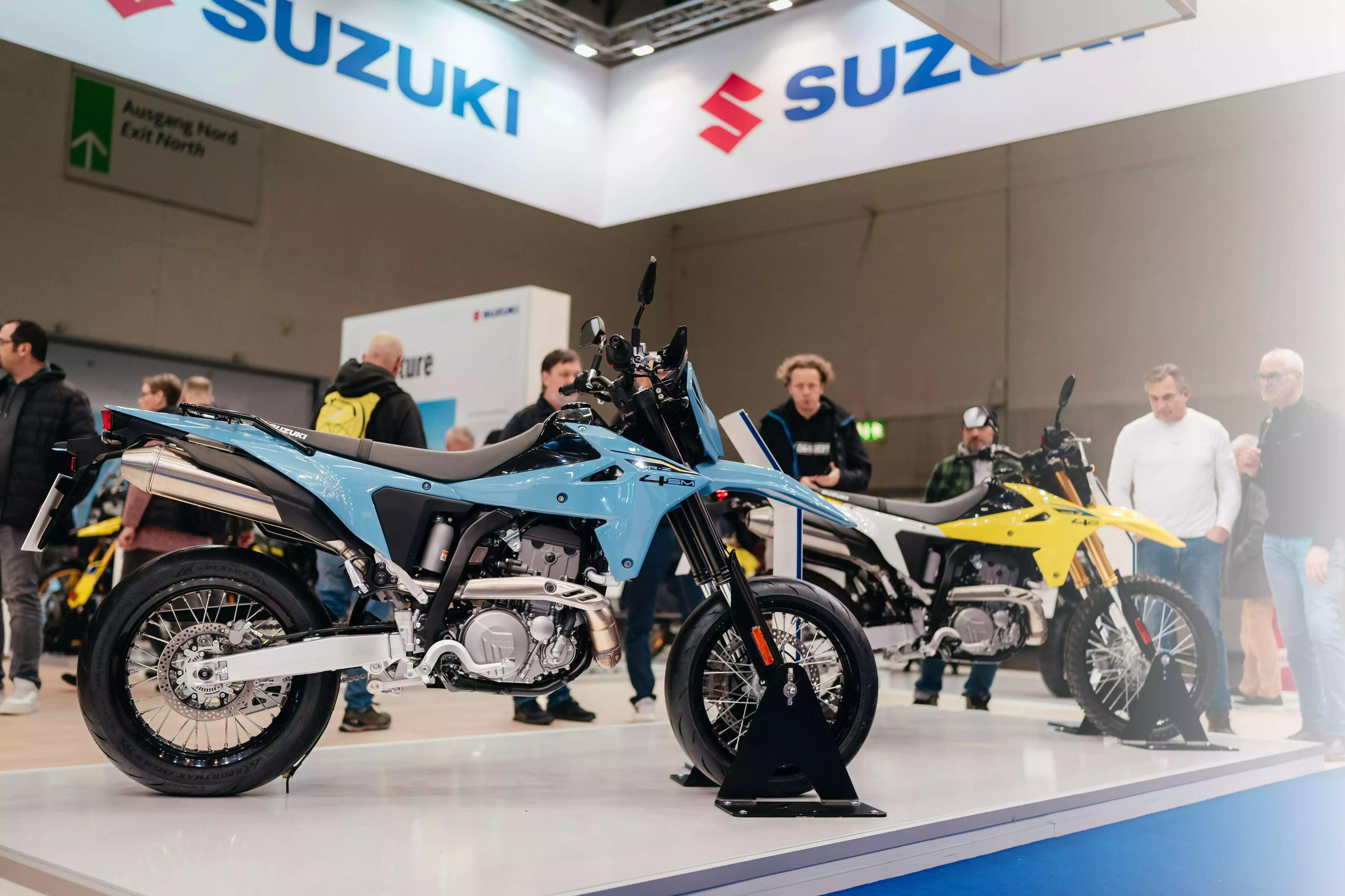 Zwei Suzuki Motorräder auf der Intermot 2024 Messe, umgeben von Besuchern.