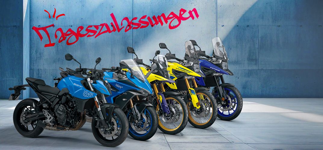 5 verschiedene Suzuki Motorradmodelle auf grauem Betonboden, leicht versetzt nebeneinander angeordnet. Eine GSX-8S und eine GSX-S1000GT in hellblauer Farbe, eine V-Strom 800DE und eine V-Strom 1050DE in gelber Farbe und eine V-Strom 1050 in dunkelblauer Farbe. Im Hintergrund eine hellblaue Wand mit Schriftzug im Graffiti-Look: "Tageszulassungen/Euro 5".