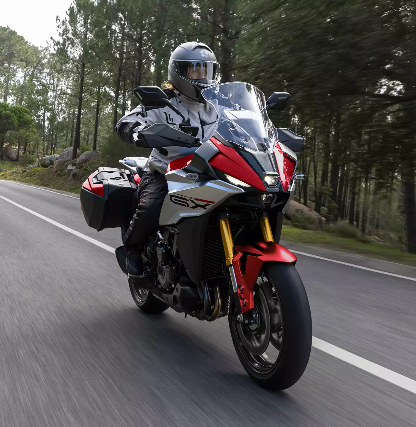 Action-Bild von der GSX-S1000GX in Rot auf einer Landstraße im Wald