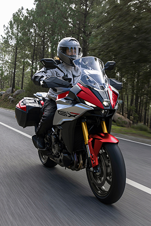 Action-Bild von der GSX-S1000GX in Rot auf einer Landstraße im Wald