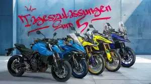 5 verschiedene Suzuki Motorradmodelle auf grauem Betonboden, leicht versetzt nebeneinander angeordnet. Eine GSX-8S und eine GSX-S1000GT in hellblauer Farbe, eine V-Strom 800DE und eine V-Strom 1050DE in gelber Farbe und eine V-Strom 1050 in dunkelblauer Farbe. Im Hintergrund eine hellblaue Wand mit Schriftzug im Graffiti-Look: "Tageszulassungen/Euro 5".
