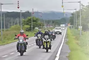 Gruppe von Suzuki Motorradfahrern in voller Montur auf Landstraße, genießt gemeinsame Fahrt auf zwei Rädern.