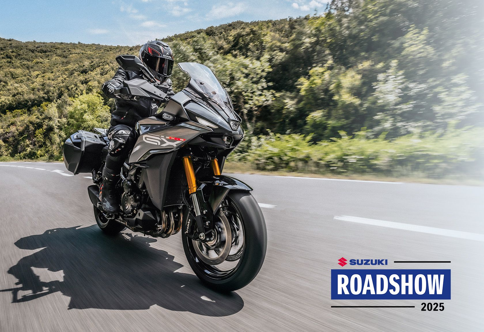Motorradfahrer auf einer Suzuki GSX-S1000GX in Fahrt durch eine kurvige Landschaft, dynamisch eingefangen bei der Suzuki Roadshow 2025. Rechts unten im Bild das Logo " Suzuki Roadshow 2025".