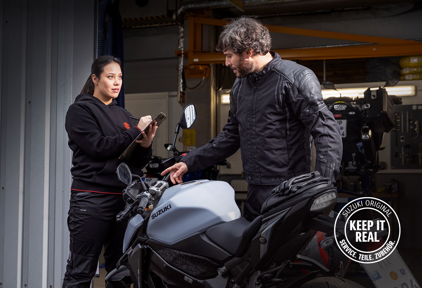 Mechanikerin und Fahrer besprechen ein Suzuki-Motorrad in der Werkstatt.