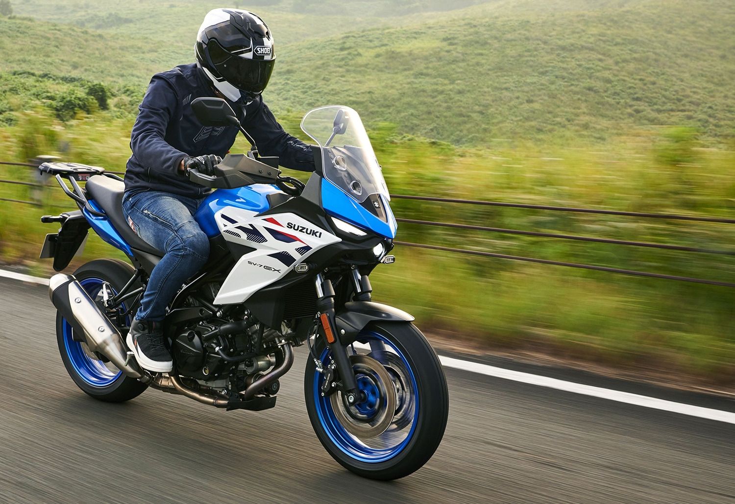 Fahrer mit Helm auf einem blau-weißen Motorrad vor Waldhintergrund