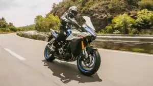 Blaue Suzuki GSX-S1000GX fährt durch eine Kurve auf einer asphaltierten Landstraße bei Tageslicht