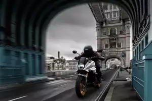 Silbergraue Suzuki Katana mit goldenen Felgen und Fahrer fährt dynamisch über eine ikonische Stadtbrücke.