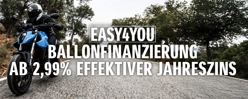 Ein Motorradfahrer auf einer blauen Suzuki GSX-8S fährt dynamisch über eine Landstraße durch bewaldetes Gelände. Im Vordergrund steht der Hinweis auf die „EASY4YOU Ballonfinanzierung ab 2,99 % effektiver Jahreszins“.