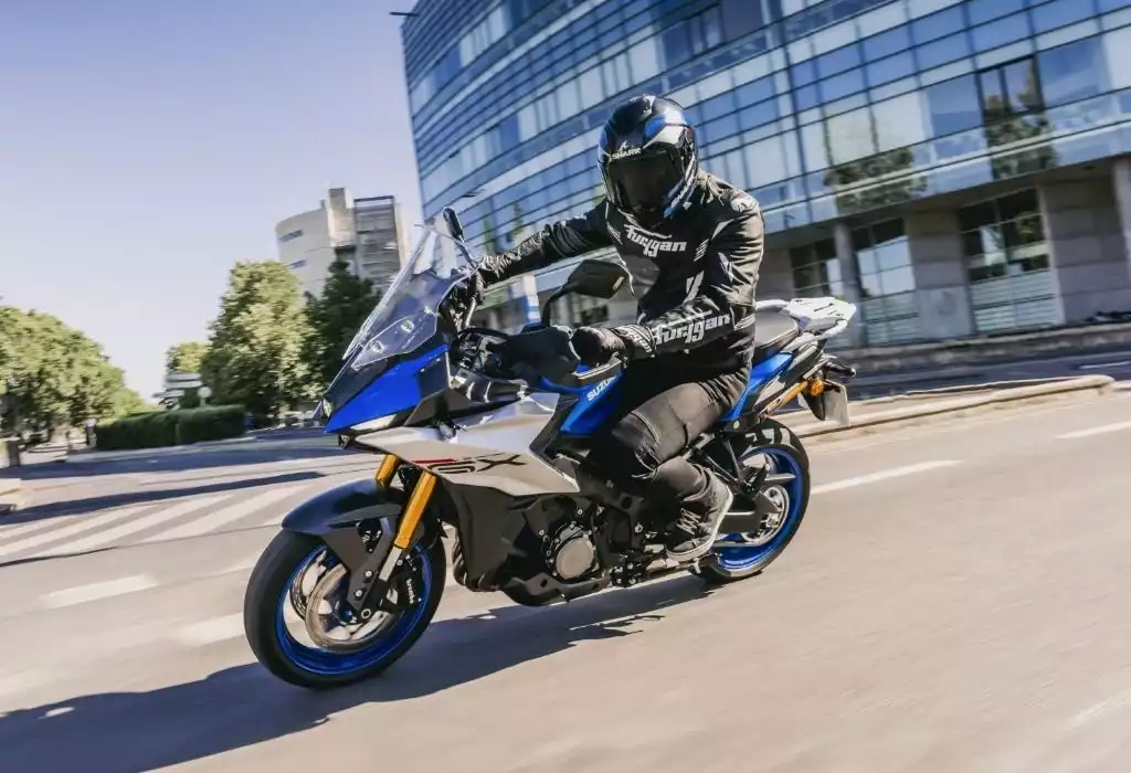 Motorradfahrer auf Suzuki GSX-S1000GT vor modernem Bürogebäude in der Stadt.