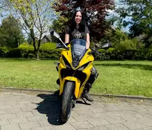 Frau sitzt lächelnd auf einer leuchtend gelben Suzuki GSX-8R, bereit für eine Motorradausfahrt.
