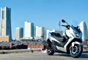 Silberner Suzuki Burgman 400 Scooter, geparkt vor einer modernen Stadtkulisse mit Hochhäusern.