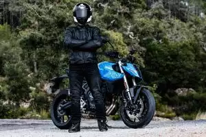 Motorradfahrer mit Helm steht neben blauer Suzuki GSX-8S in natürlicher Umgebung.