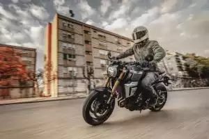 Fahrer auf grauer Suzuki GSX-8T mit goldenen Gabeln in dynamischer Kurvenfahrt durch die Stadt.