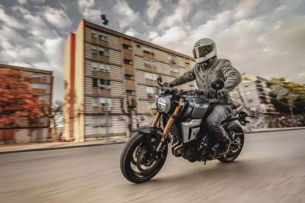 Fahrer auf grauer Suzuki GSX-8T mit goldenen Gabeln in dynamischer Kurvenfahrt durch die Stadt.