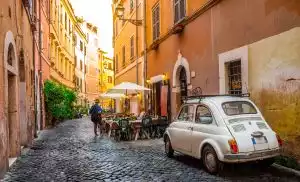Ein malerisches italienisches Dorf, im Vordergrund ein alter Fiat 500 und dahinter ein Restaurant mit Außengastronomie