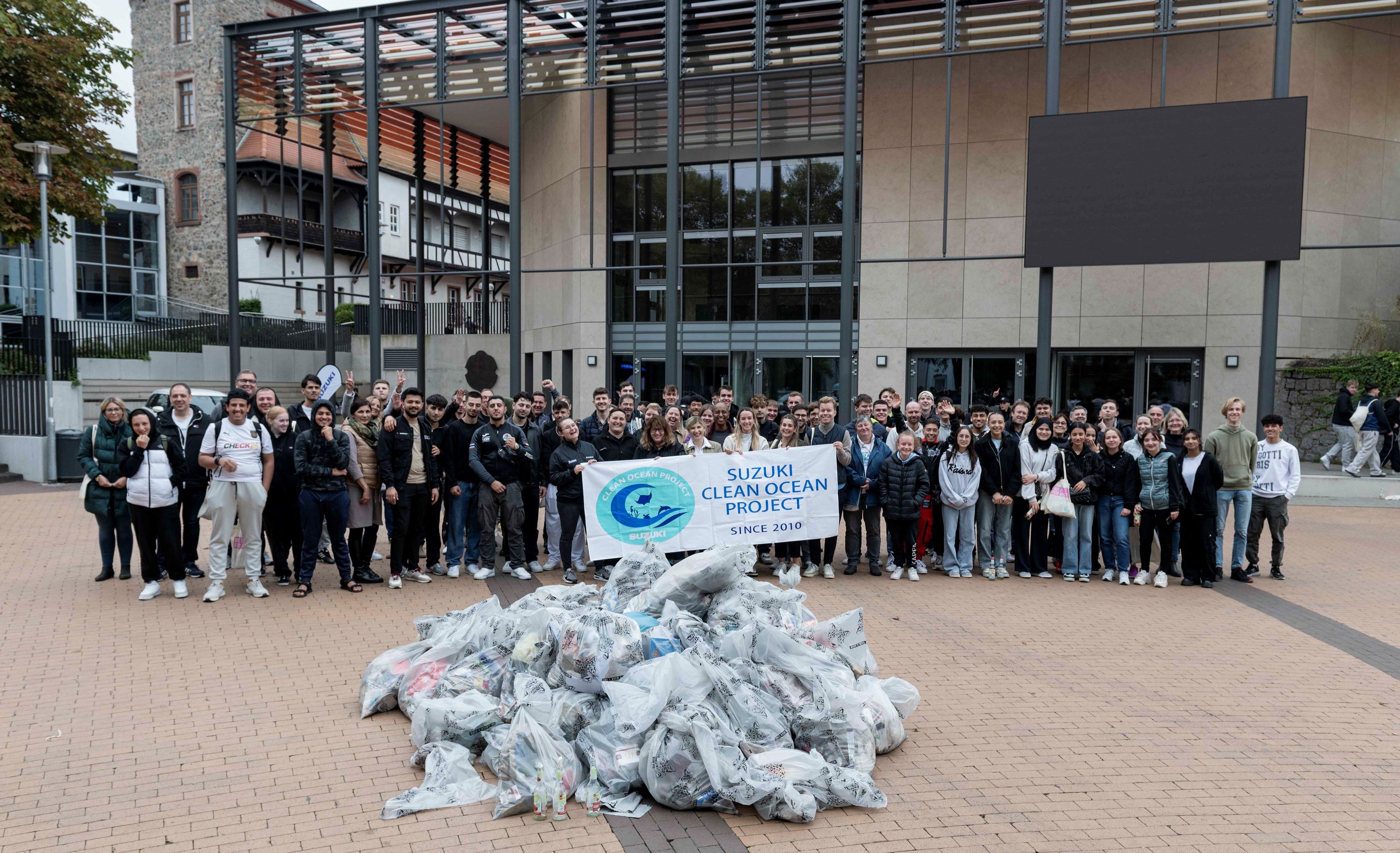 Gruppenfoto von vielen Menschen vor einem Gebäude, die im Rahmen des ‚Suzuki Clean Ocean Project‘ gesammelten Müll in Plastiksäcken präsentieren