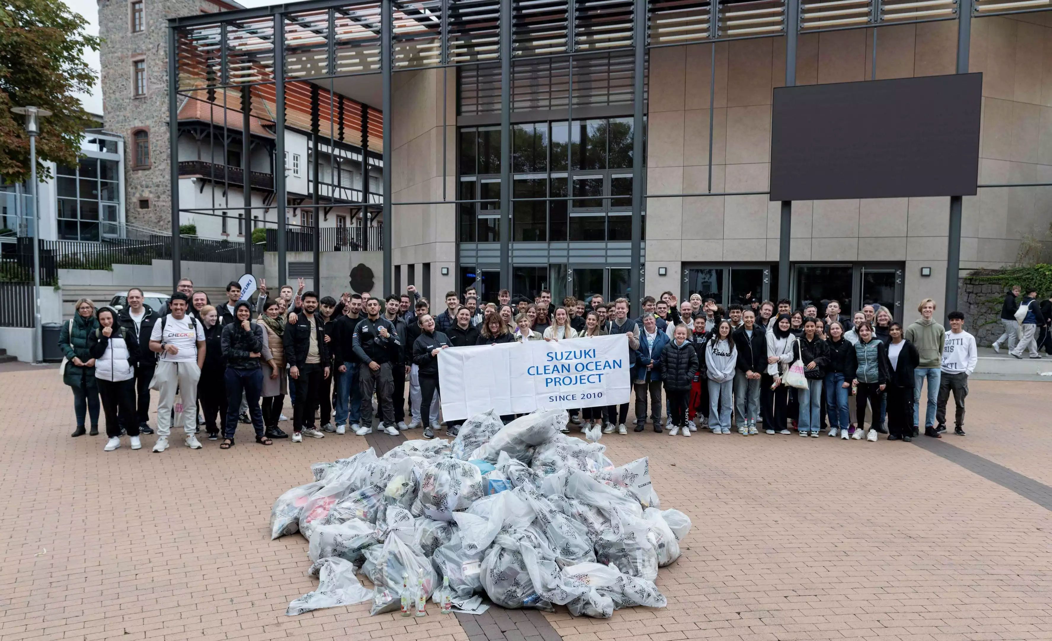 Gruppenfoto von vielen Menschen vor einem Gebäude, die im Rahmen des ‚Suzuki Clean Ocean Project‘ gesammelten Müll in Plastiksäcken präsentieren