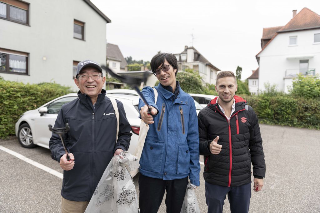 Drei Männer mit Müllzangen und Sammelbeuteln lächeln in die Kamera bei einer Aufräumaktion