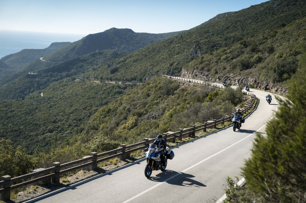 Gruppe von Motorradfahrenden auf Suzuki-Motorrädern fährt eine kurvige Bergstraße mit weitem Blick über grüne Hügel und das Meer
