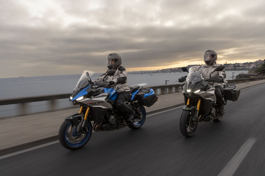 Zwei Motorradfahrende auf Suzuki-Motorrädern fahren bei Sonnenuntergang am Meer entlang