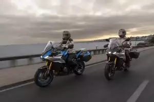 Zwei Motorradfahrende auf Suzuki-Motorrädern fahren bei Sonnenuntergang am Meer entlang