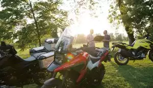 Motorradfahrer bei Gruppenfahrt im Grünen mit Suzuki Adventure-Modellen im Sonnenlicht.
