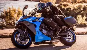 Zwei Motorradfahrer auf einer blauen Suzuki GSX-S1000GT auf einer kurvigen Straße.