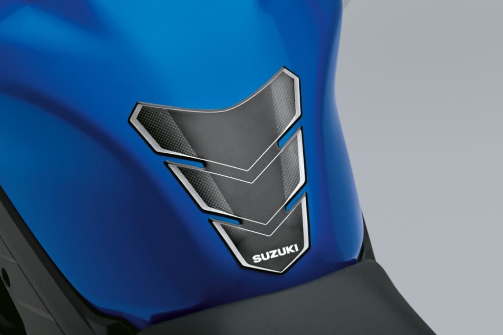 Schwarzer Tankpad-Schutz mit karbonähnlicher Struktur auf einem blauen Kraftstofftank; Suzuki-Logo am unteren Rand.