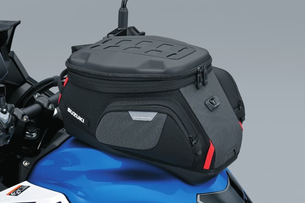Große schwarze Tanktasche von Suzuki, montiert auf einem blauen Tank; robustes Design mit seitlichen Reflexelementen und Reißverschlüssen.