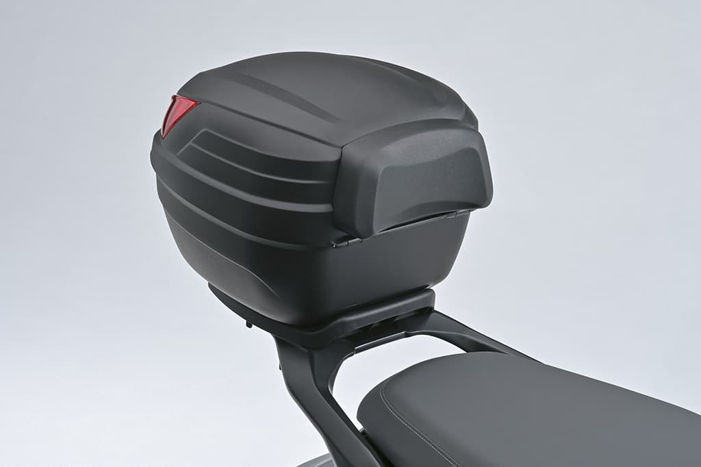 Schwarzes Topcase mit Rückenpolster, montiert am Heck eines Suzuki e-Address Elektrorollers, vor hellem Studiohintergrund.