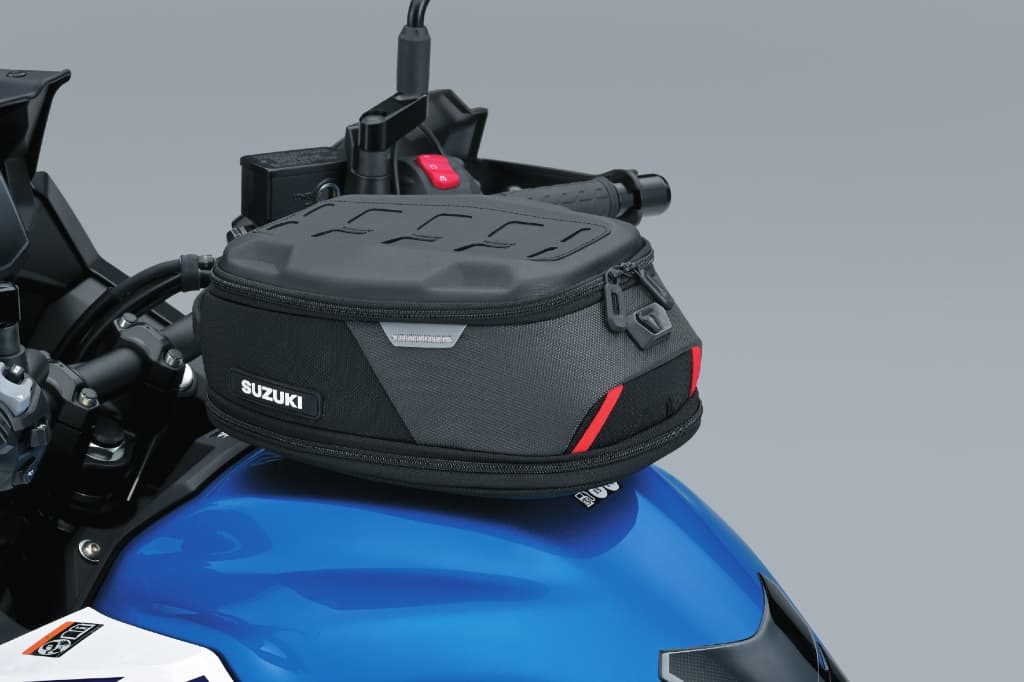 Kompakte schwarze Tanktasche von Suzuki auf einem blauen Tank; flaches, aerodynamisches Design mit seitlichen roten Akzenten.