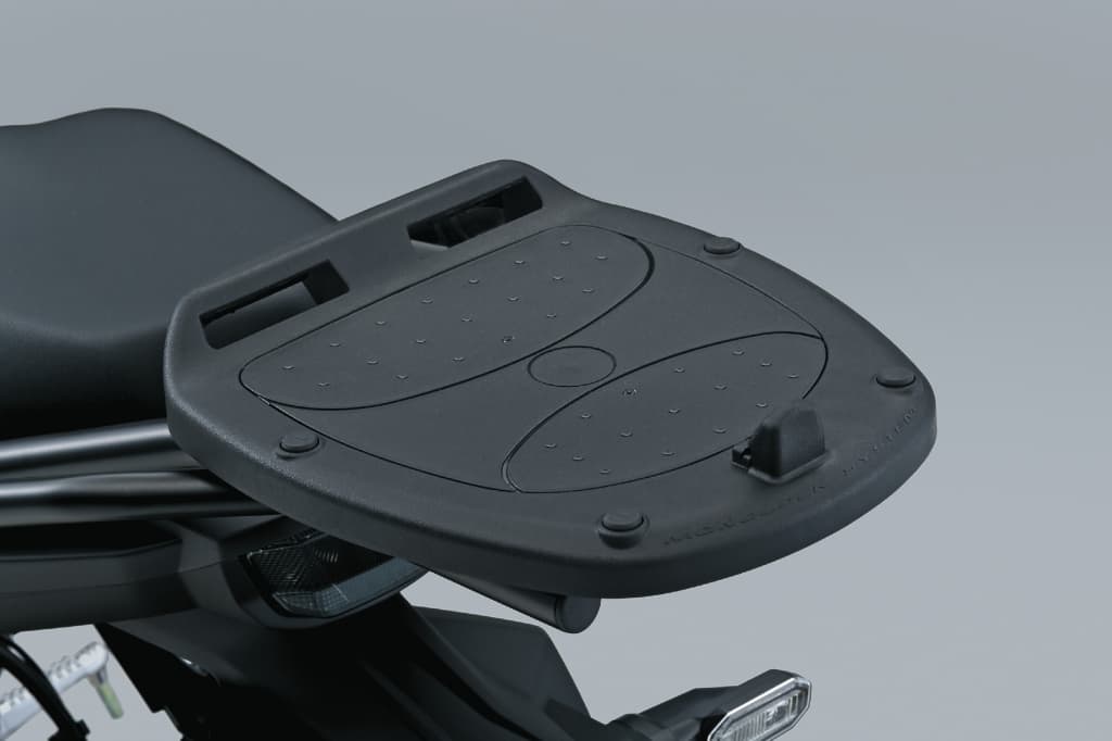 Schwarze Topcase-Adapterplatte für Suzuki-Motorräder, montiert hinter der Sitzbank; strukturierte Oberfläche mit Befestigungspunkten.