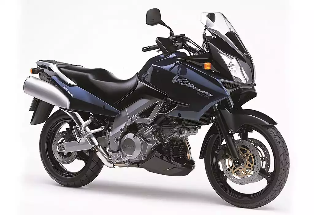 Eine Suzuki V-Strom 1000 aus dem Jahr 2002 steht vor weißem Hintergrund. Das Motorrad ist schwarz-blau, besitzt einen markanten Windschutz, große Scheibenbremsen und einen kräftigen Auspuff. Die Maschine wirkt robust und ist für lange Touren konstruiert.