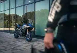 Blaues Suzuki-Motorrad vor modernem Gebäude, Fahrer im Vordergrund