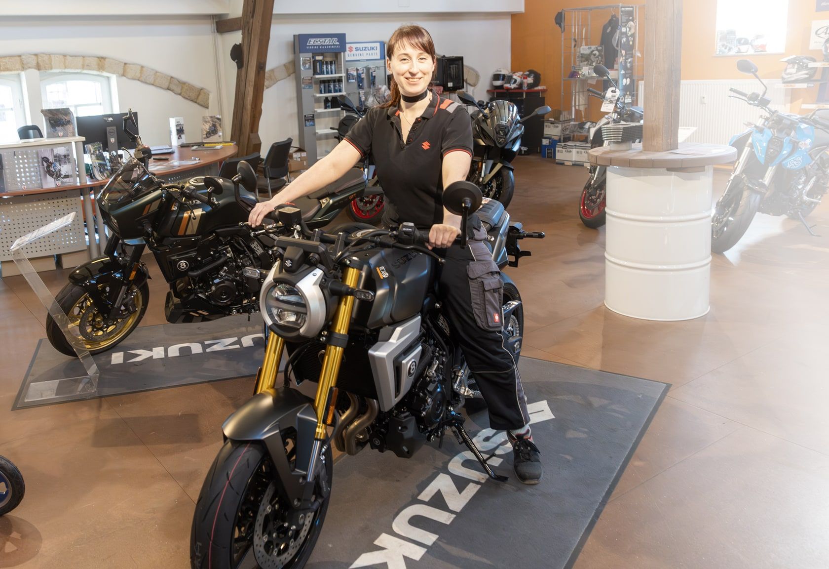 Frau im Suzuki-Motorradzentrum präsentiert ein neues Naked Bike im Ausstellungsraum mit mehreren Motorrädern im Hintergrund