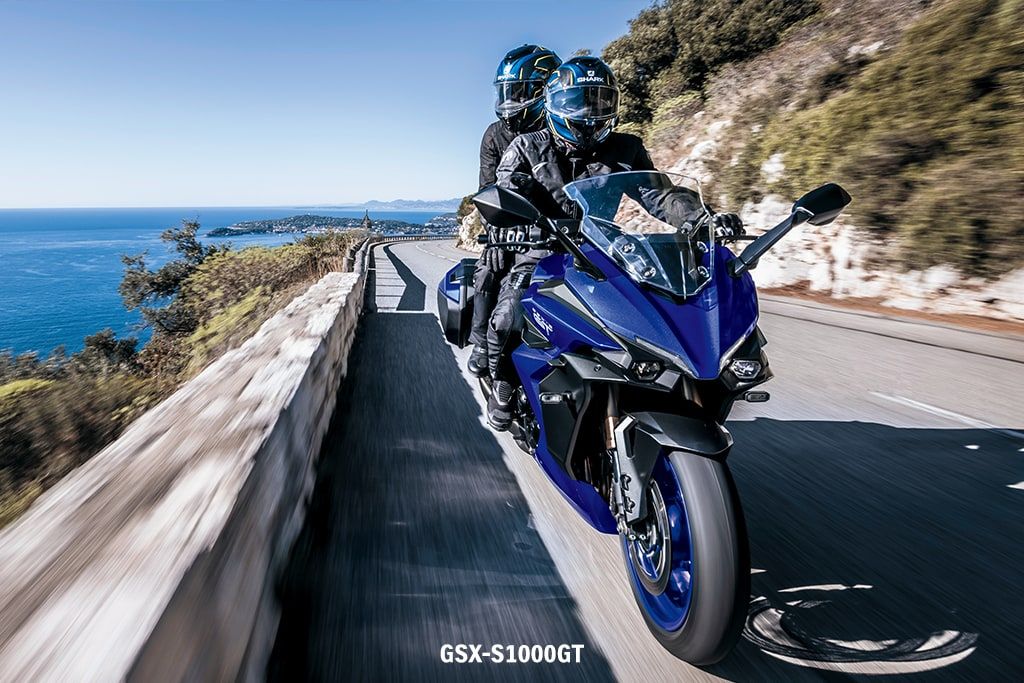 Blaue Suzuki GSX-S1000GT an einer Küstenstraße, ein Fahrer mit Beifahrer in Motorrad-Outfit