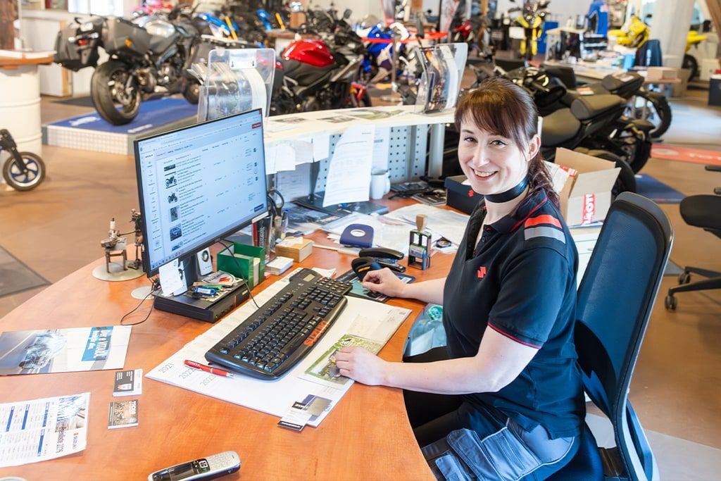 Eine Frau im Suzuki-Motorradhandel arbeitet am Computer im Büro, im Hintergrund stehen mehrere ausgestellte Motorräder