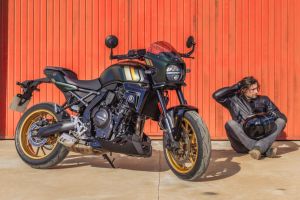 Dunkelgrüne Suzuki GSX-8TT mit goldenen Felgen vor rotem Hallentor, daneben ein sitzender Motorradfahrer mit Helm