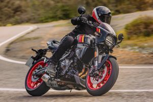Ein Motorradfahrer in Schräglage auf einer schwarzen Suzuki GSX-8TT mit roten Felgen auf einer asphaltierten Landstraße.