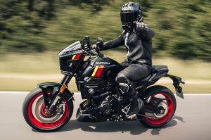 Ein Fahrer in schwarzer Lederkombi fährt auf einer schwarzen Suzuki GSX-8TT mit roten Felgen und zeigt mit dem Finger dynamisch nach vorne.