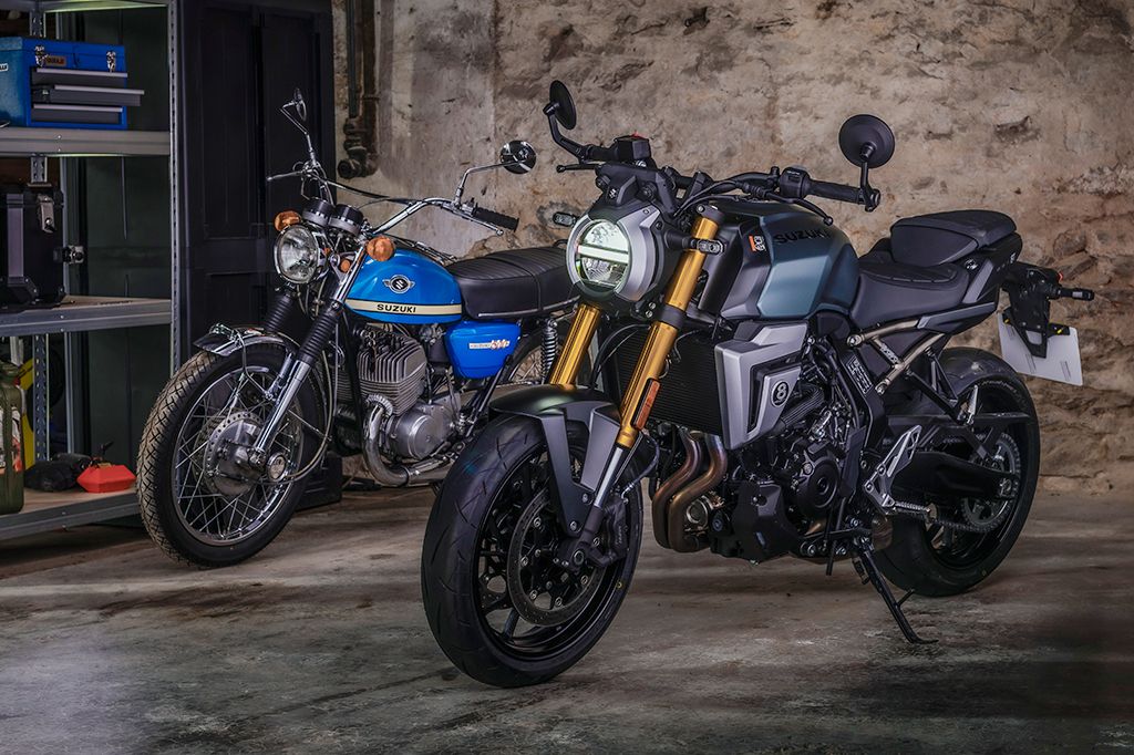 Zwei Suzuki Motorräder nebeneinander in einer Werkstatt: Eine moderne, mattsilberne GSX-8T im Vordergrund und eine blau-weiße T500 im Hintergrund.