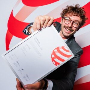 Lead Designer Arthur Vidal im Anzug hält stolz die gerahmte „Red Dot Winner 2026“-Urkunde für die Modelle GSX-8T/TT in die Kamera.